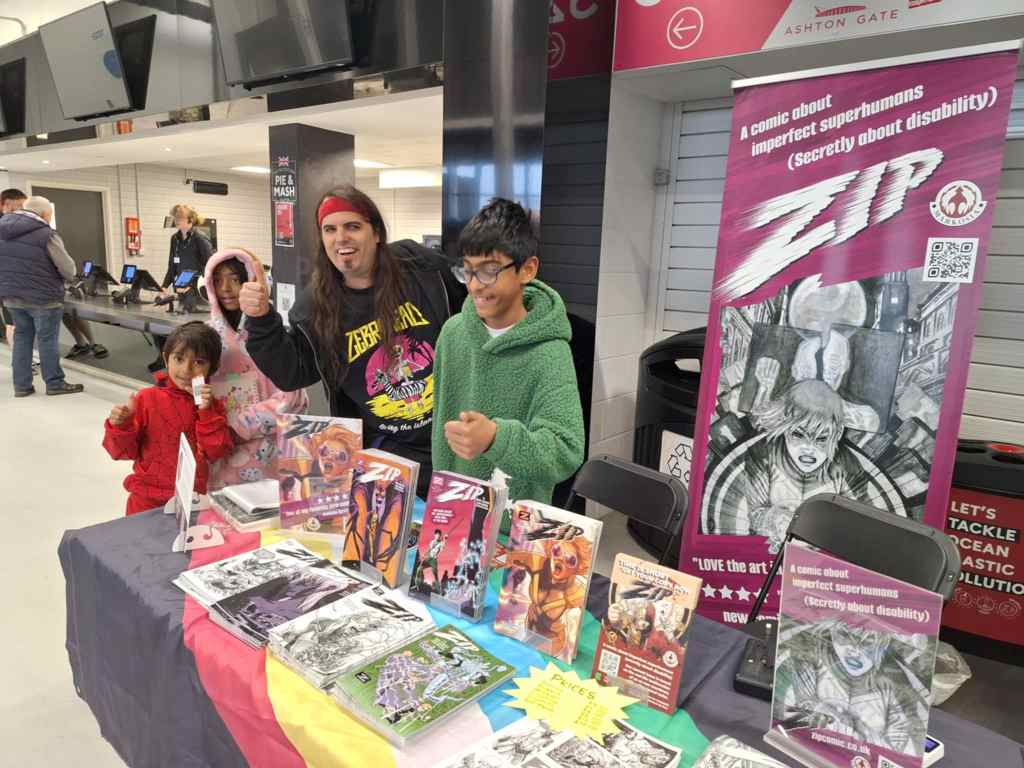 Photo of writer Mike Scrase giving a thumbs up with some young Zip readers (ages 8 to 12) behind our table at Bristol Comic-Con.